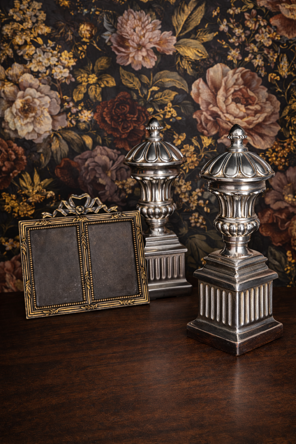 Decorative silver urns and a gold frame against a floral wallpaper background
